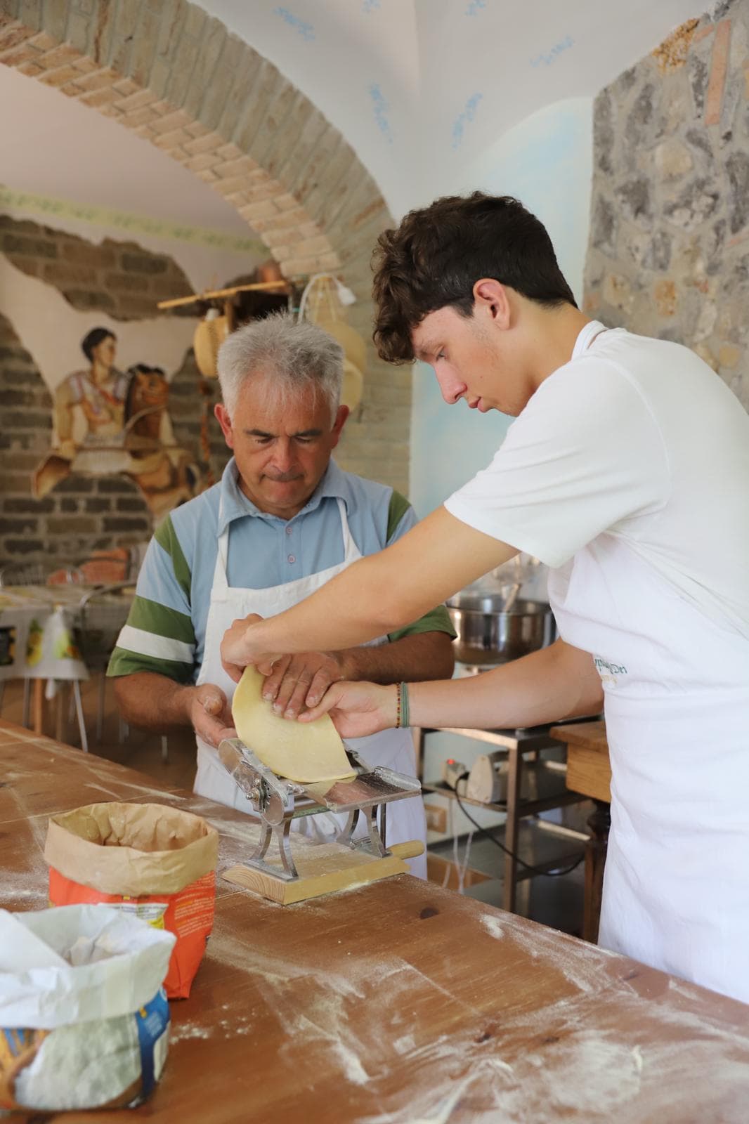 Rolling fresh pasta dough through a hand crank in the family's vaulted stone cellar