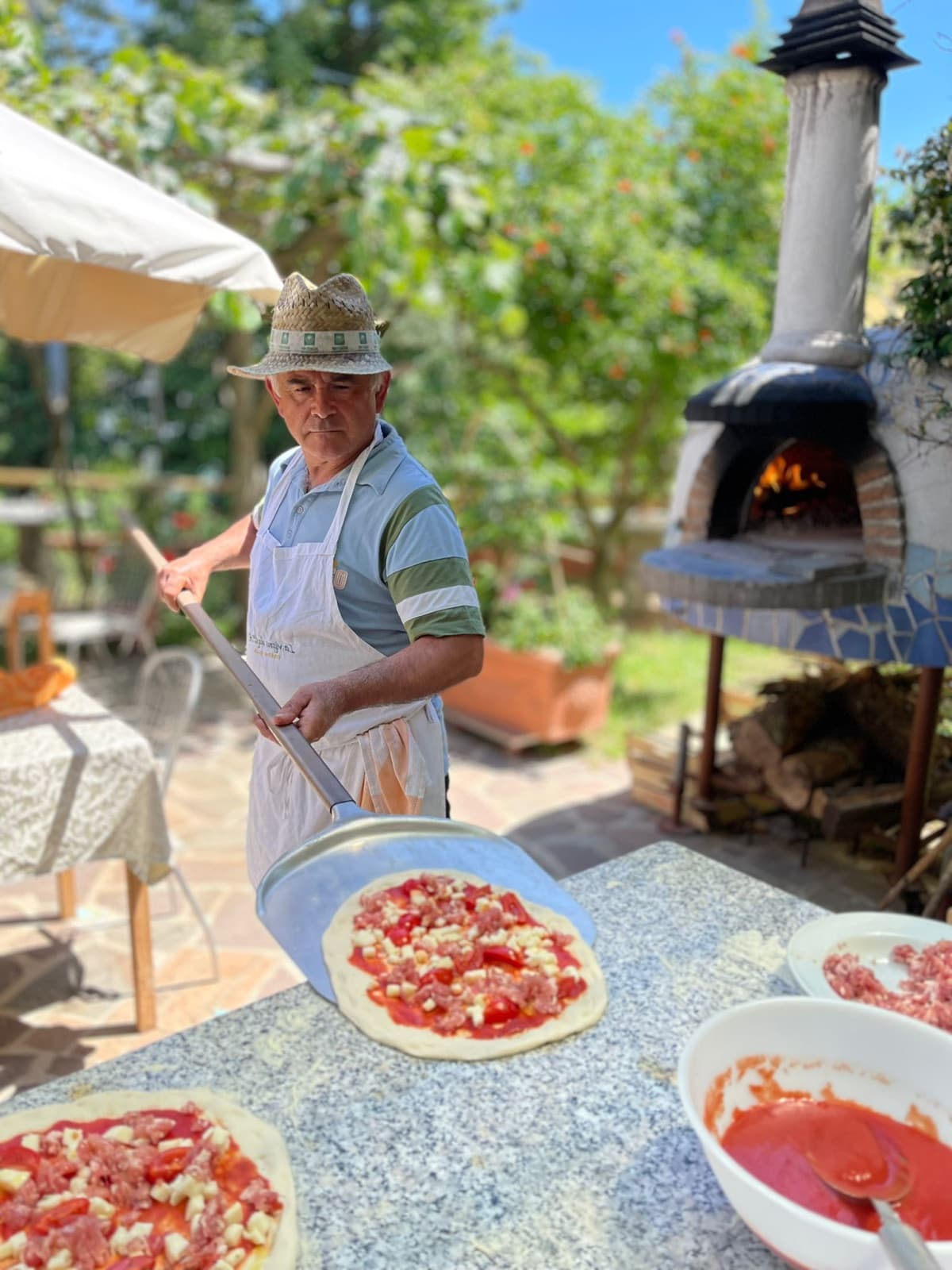 Pasquale sliding a topped pizza into the wood-fired oven in the garden